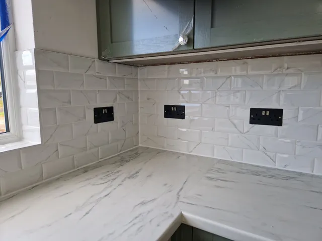 White marble-effect metro tile splashback above white worktop with sage green wall units