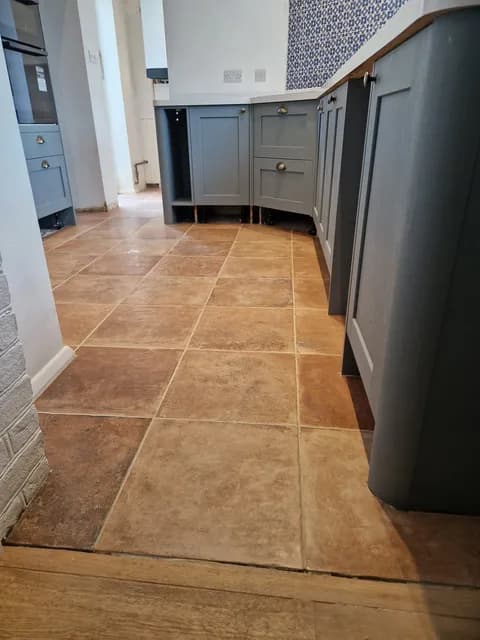 Terracotta square ceramic floor tiles with wide grout joints in a kitchen with grey units