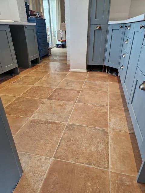 Terracotta square floor tiles running through a kitchen with blue-grey shaker cabinets