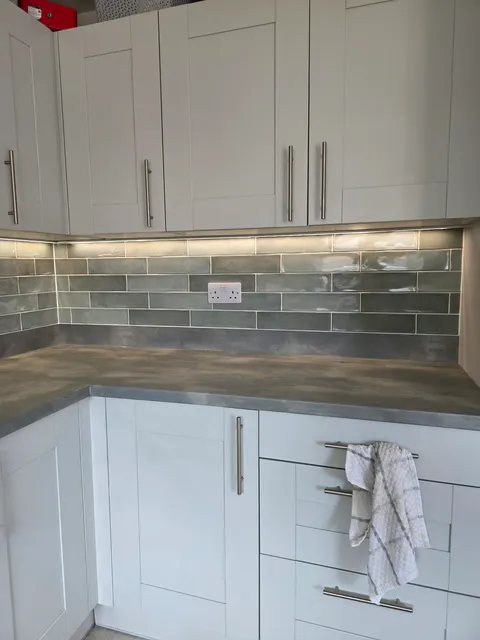 Grey gloss metro tile splashback under-cabinet lighting with white shaker units and stone worktop