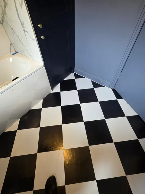 Black and white checkerboard LVT flooring in a bathroom beside a marble bath panel