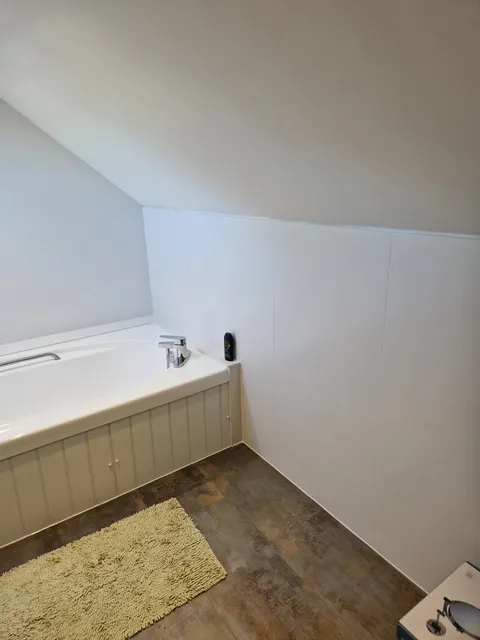 White-panelled bath with white wall panelling and dark wood-effect flooring under a sloped ceiling