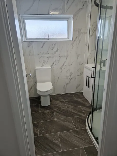 White marble-effect wall tiles with toilet, quadrant shower and dark wood-effect tiled floor