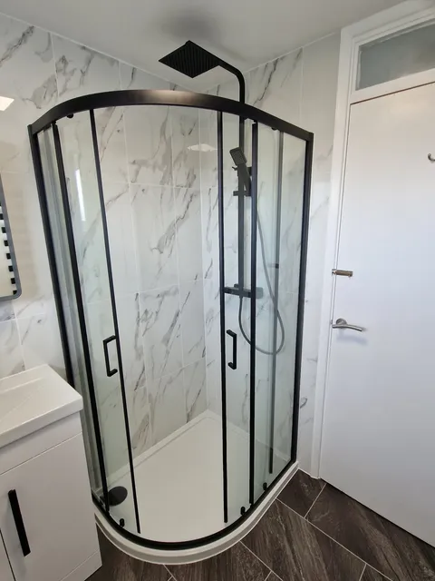 White marble-effect tiles with black-framed quadrant shower enclosure and white vanity unit