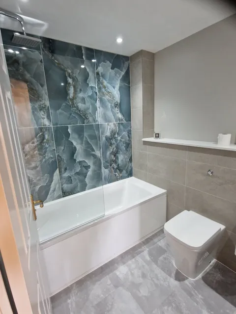 Blue onyx-effect feature wall above a bath with beige tiles, wall-hung toilet and grey marble floor