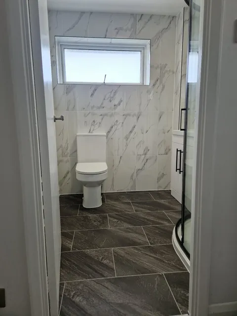 Grey marble-effect LVT flooring in a bathroom with marble walls and a corner shower