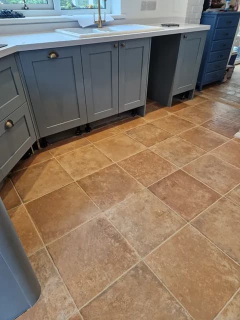 Aged terracotta square floor tiles with grout lines beneath grey shaker kitchen units
