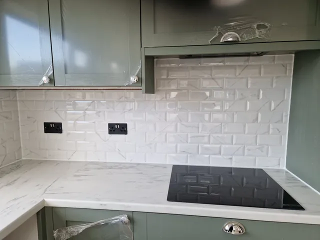 White bevelled marble-effect metro splashback behind hob with sage green cabinets and marble worktop