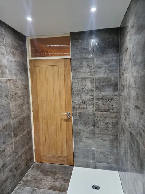 Grey concrete-effect tiled wet room walls with white shower tray and oak panelled door