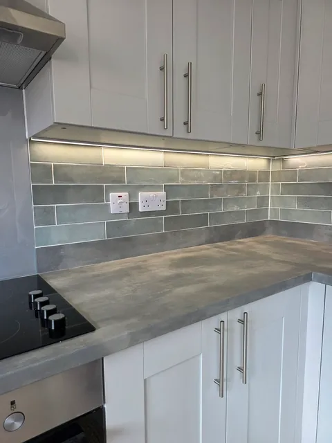 Grey-green gloss brick tile splashback behind hob with white units and grey worktop
