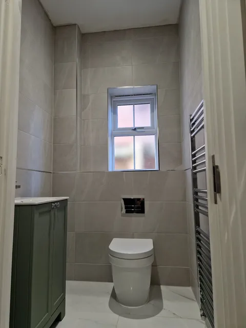 Cream marble-effect wall tiles with wall-hung toilet, green vanity and chrome towel rail