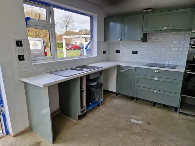 White metro tile splashback wrapping a corner with sage green shaker units and pale worktop