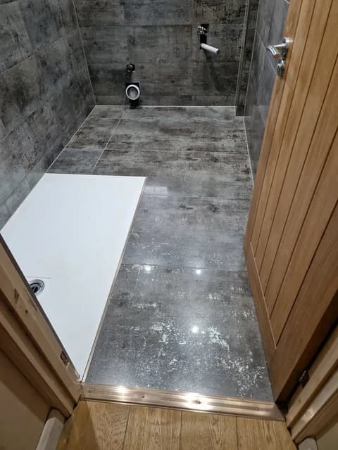 Grey concrete-effect plank porcelain floor tiles being laid beside a white shower tray