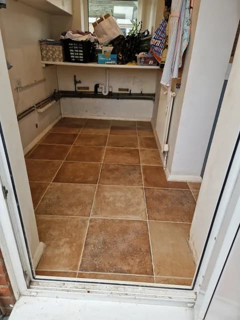 Terracotta square floor tiles with grout lines running through a utility room doorway