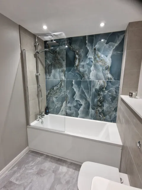 Blue onyx-effect feature wall above a bath with grey tiles, shower and grey marble-effect floor